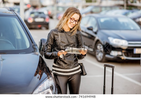 Young woman looking on the rental\
contract standing outdoors on the airport car\
parking
