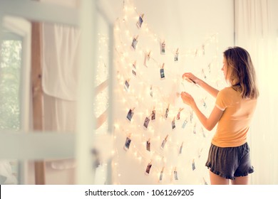 A Young Woman Looking At Photos Hanging On Decoration Lights 