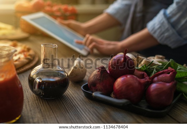 The young woman looking recipe in a tablet
computer in kitchen. Healthy food. Healthy lifestyle. Cooking at
home. Cooking according to recipe on tablet screen. Technology
concept. Toned image.