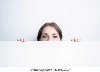 Young Woman Looking To The Side Looking Out From Under A White Table Against A White Wall.