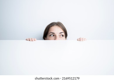 Young Woman Looking To The Side Looking Out From Under A White Table Against A White Wall.