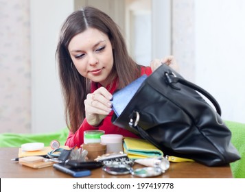 Young Woman Looking For Something In Her Purse At Table In Home