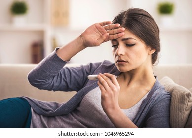 Young woman is looking at the thermometer. She has fever. - Shutterstock ID 1046965294