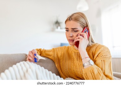 Young woman is looking at the thermometer. She has fever, calling her doctor. Beautiful woman with symptoms called covid-19 emergency number to report her medical conditions - Shutterstock ID 2240776777
