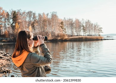 Young woman looking through binoculars at birds on the lake. Birdwatching, zoology, ecology. Research in nature, observation of animals Ornithology autumn bird migration selective focus