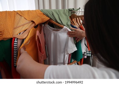 Young Woman Looking Through Clothes On Rack In Room. Fast Fashion