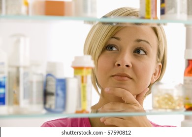 A Young Woman Is Looking Through Her Medicine Cabinet. Horizontal Shot.