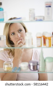 A Young Woman Is Looking Through Her Medicine Cabinet.  Vertical Shot.