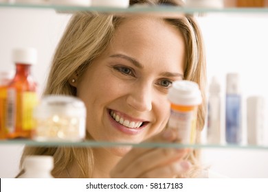 A Young Woman Is Looking Through Her Medicine Cabinet And Smiling.  Horizontal Shot.