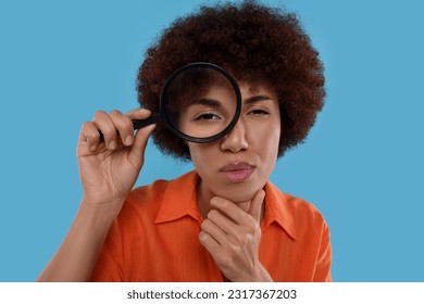 Young woman looking through magnifier glass on light blue background - Shutterstock ID 2317367203