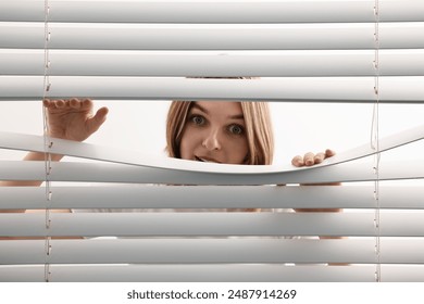 Young woman looking through window blinds on white background - Powered by Shutterstock