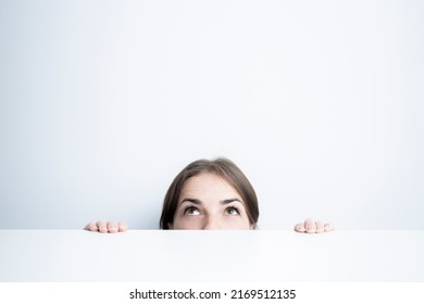 Young Woman Looking Up From Under A White Table Against A White Wall.