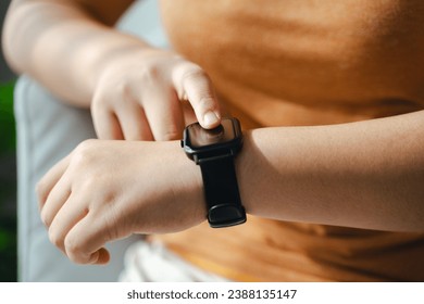 young woman looking and using a smartwatch, Female sitting on the sofa checking her smartwatch. - Powered by Shutterstock