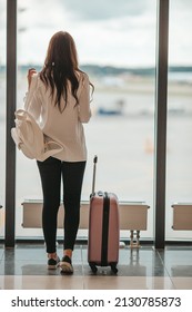 Young woman looking at the window in an airport lounge waiting for flight aircraft