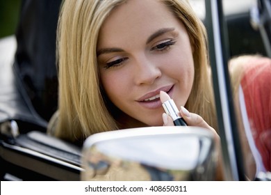 A young woman looking in the wing mirror of her car applying lipstick - Powered by Shutterstock