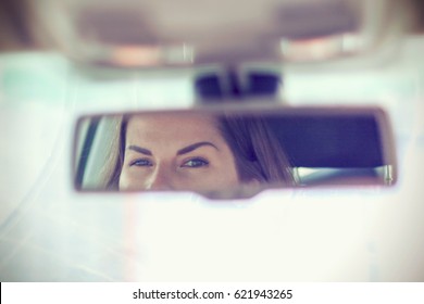 Young Woman Looks In The Car Rearview Mirror