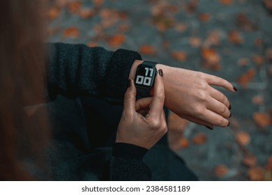 Young woman looks at his wristwatch and checks the time. Girl in the park in autumn. Time on the clock 11-00
