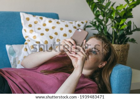 Young woman looks into the smartphone screen while lying on the couch. FOMO - Fear Of Missing Out