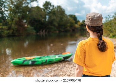 A young woman looks at a kayak. Rear view. Copy space. The concept of kayaking and outdoor activities.