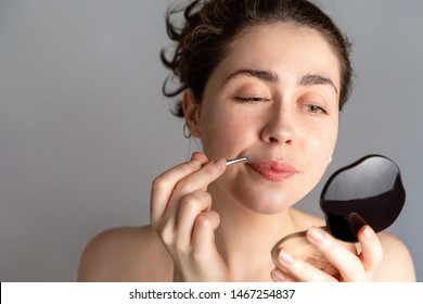 A Young Woman Looks In The Mirror And Plucks Her Hair Over Her Upper Lip With Tweezers. The Concept Of Getting Rid Of Unwanted Facial Hair