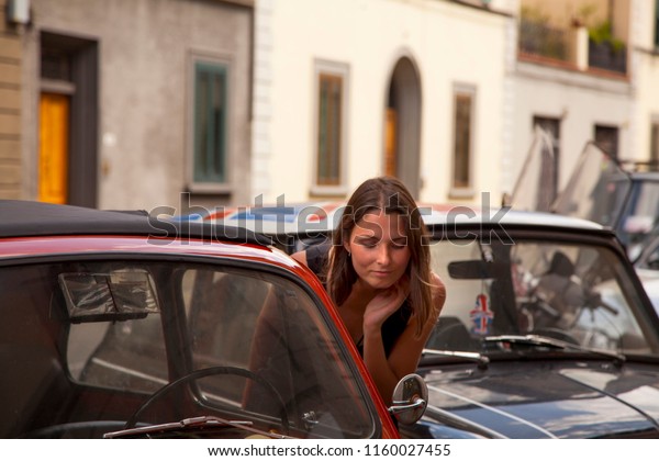 Young woman looks at mirror of vintage car,\
Florence, Italy