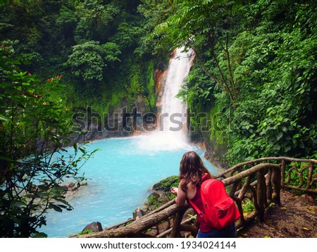 Young woman looks out over a picturesque rain forest waterfall in Costa Rica.
