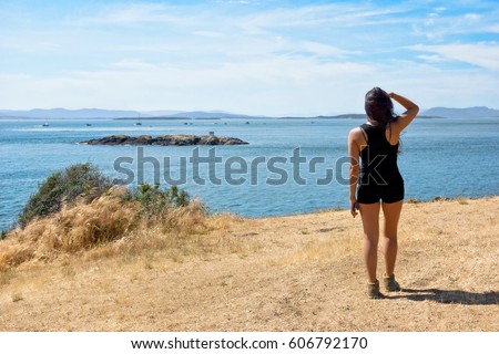 Young woman looks out over the Haro Strait and sees a family of Orcas.