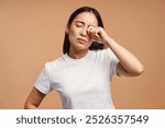 Young woman looks sad and upset, rubbing her eyes as if crying. She shows emotional pain, stress, and anxiety, reflecting loneliness and sorrow