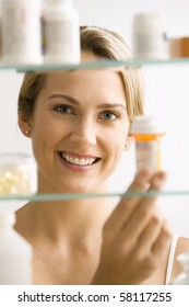 A Young Woman Looks Through A Medicine Cabinet And Smiles At The Camera.  Vertical Shot.