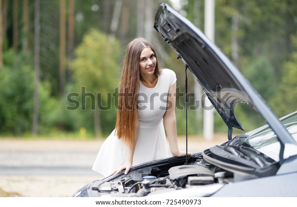 Young woman looks under the hood of his car, which\
broke down