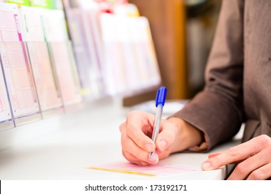 Young Woman In A Lotto Store Playing Lottery Ticket To Win With Luck, She Fills The Ticket With A Pen