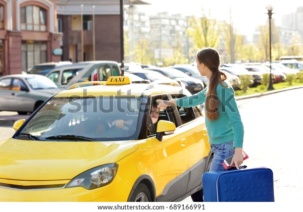 Young woman\
with luggage catching taxi on\
street