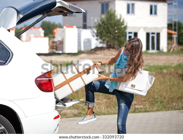 Young woman with luggage. Happy woman taking off\
suitcases from the car trunk.\
