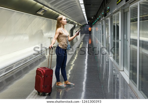 Young woman with luggage waiting train in
platform of subway
station