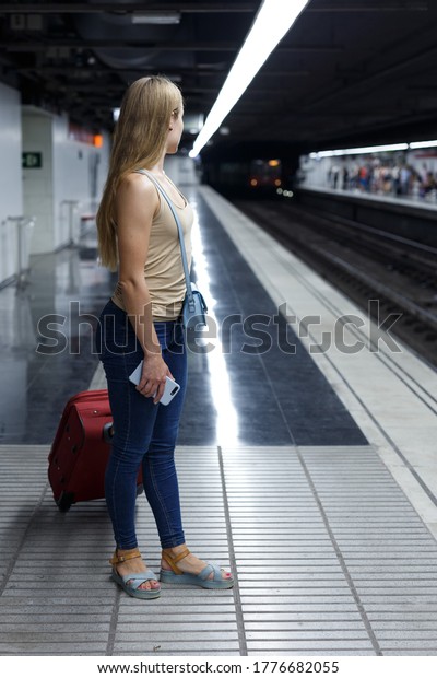 Young woman with luggage waiting train in\
platform of subway\
station