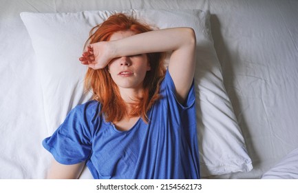 young woman lying in bed with migraine and sensitivity to light covering her eyes