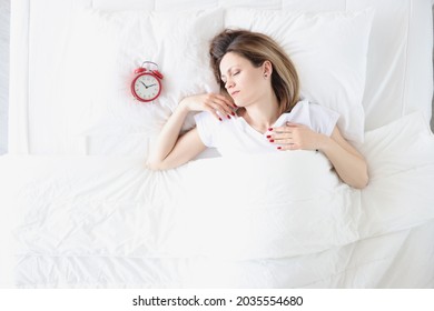Young woman lying in bed near red alarm clock top view - Shutterstock ID 2035554680