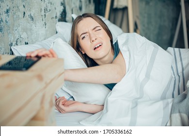 Young Woman Lying In Bed And Opening One Eye To Get Her Ringing Phone In The Morning