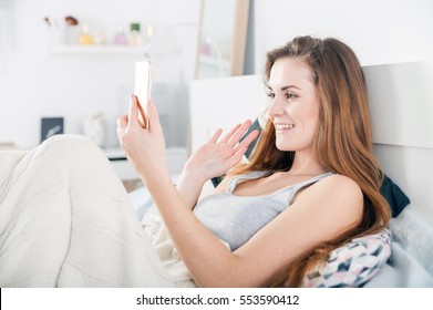 Young woman lying in bed and video calling on smart phone