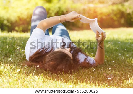 young woman lying down on grass reading a book