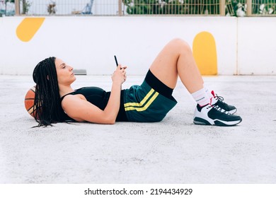 Young Woman Lying Down Using A Smart Phone And A Basketball On Court