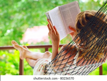 Young woman lying in hammock in a garden and reading a book. Shallow DOF. Focus on a left shoulder - Powered by Shutterstock