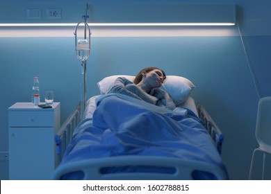 Young Woman Lying In A Hospital Bed At Night And Sleeping With IV Drip