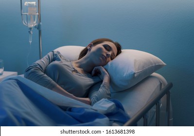 Young Woman Lying In A Hospital Bed At Night And Sleeping With IV Drip