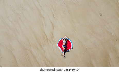 Young Woman Lying On The Beach Blanket, Sunbather On White Sand, Top View From Flying Drone.