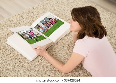 Young Woman Lying On Carpet Looking At Family Photo Album