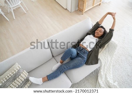 Young woman lying on comfy sofa. Smiling girl stretching body awaking after sleep on cozy couch breath fresh air inside modern living room, enjoying leisure, break, weekend. Recreation, stress relief.
