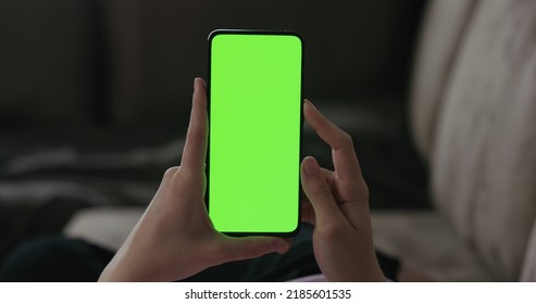 Young woman lying on a couch and using smartphone with vertical green screen, wide photo - Powered by Shutterstock