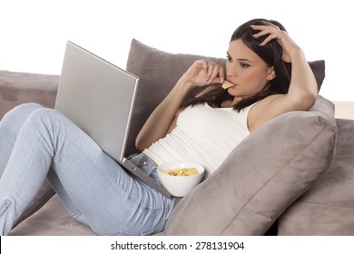 Young Woman Lying On The Couch With A Laptop In Front Of Her And Eating Potato Chips