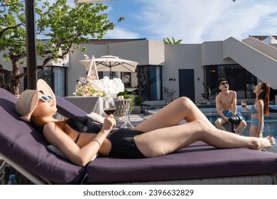 Young woman lying on the deck chair beside the swimming pool to drink red wine - Powered by Shutterstock